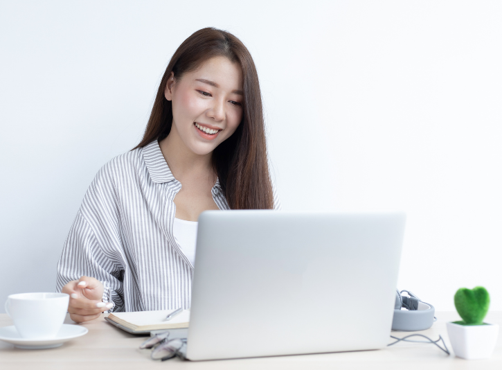 Marketing consultant smiling and looking at laptop for zoom meeting with small business client with coffee and plant on desk